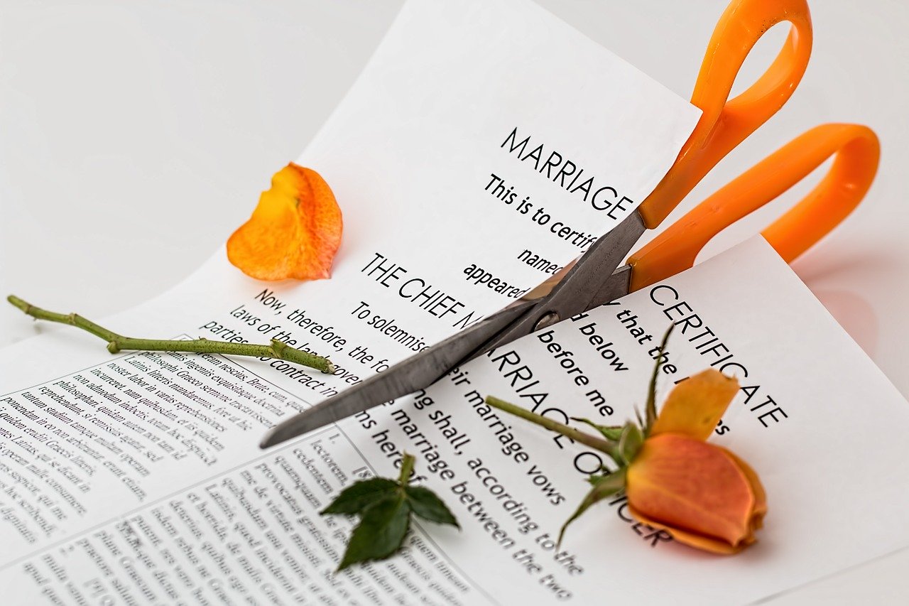 Scissors cutting through a marriage certificate and orange rose
