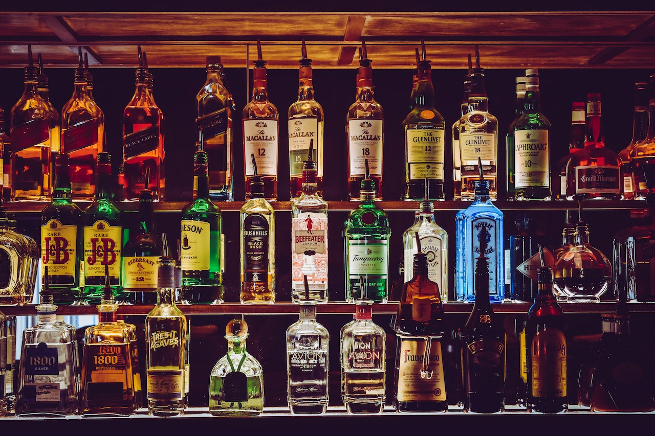 A variety of alcohol bottles lined up on a shelf in a bar.